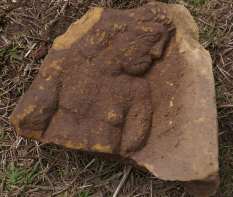 Carved sandstone figure found at Caerleon 2010. (Image courtesy of excavation team.) The right edge of this is the original unbroken side. So the figure would appear to be stooping, in addition he looks deep in thought and his left arm seems to be tied behind his back. Mark Lewis, of the Roman Legion Museum Caerleon, thinks this could be a god/hero figure or perhaps a bound captive. A bound captive seems to fit the bill. It was found amongst rubble which had been used in one of the later phases.